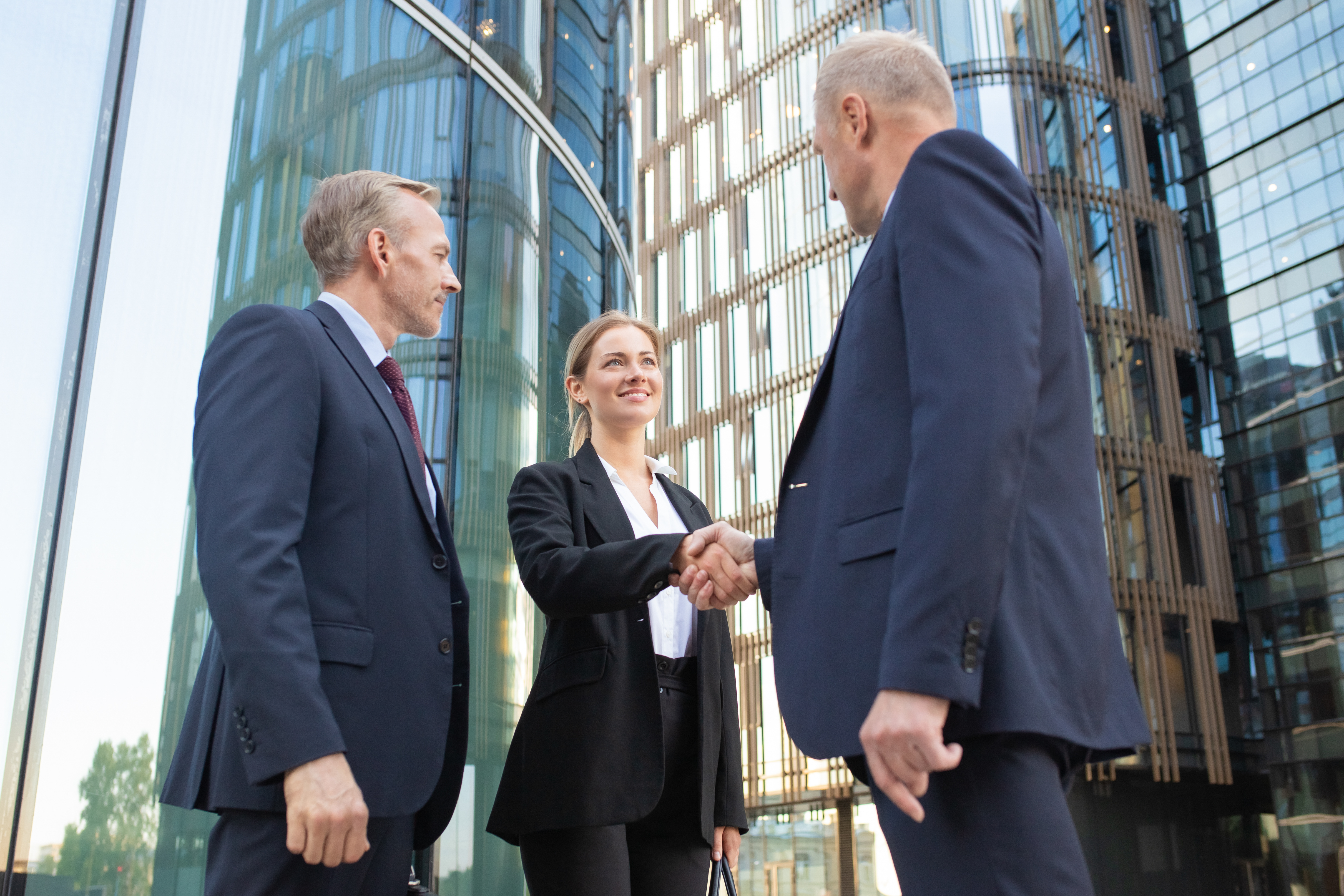 Three business people shaking hands in front of an office building.