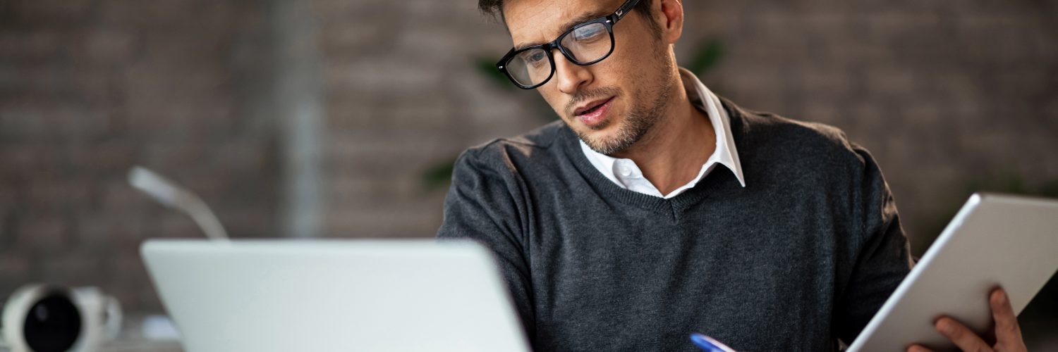 A man wearing glasses focused on his laptop screen, engrossed in his work.