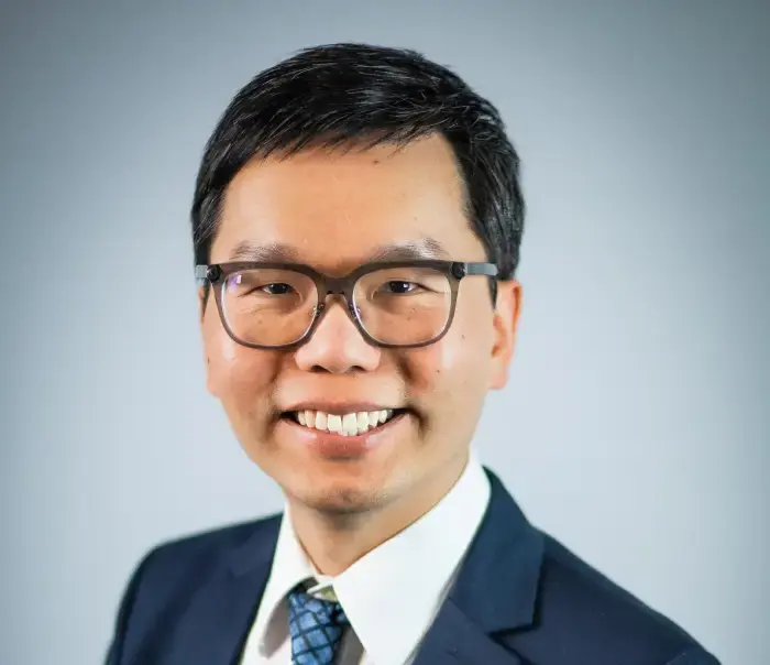 A professional Asian man wearing a suit and tie with a warm smile on his face.