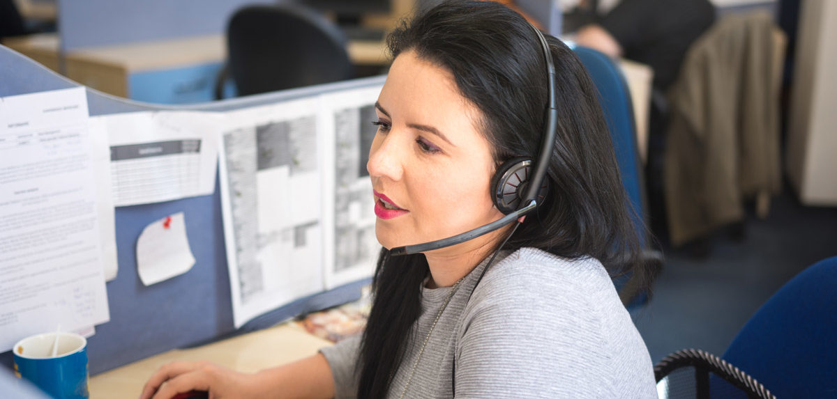 A woman wearing a headset, working in an office environment, assisting customers or engaging in telecommunication activities.
