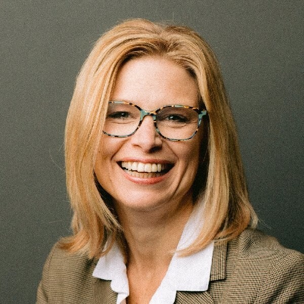 A professional woman wearing glasses and a suit, smiling confidently.