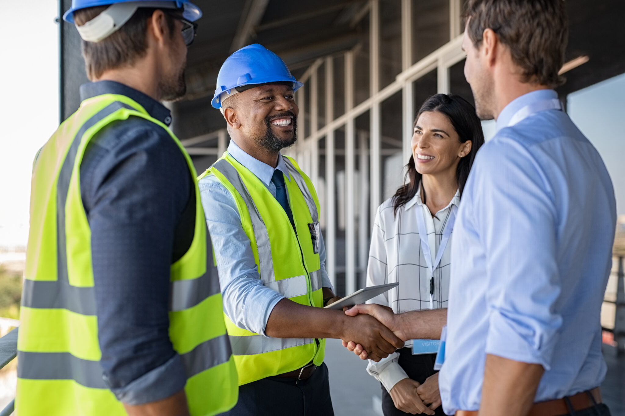 Three individuals in hard hats exchanging handshakes, symbolizing a successful collaboration in a construction setting.